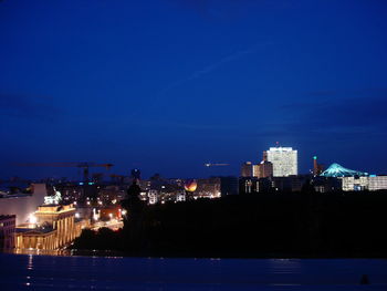 Illuminated buildings by river against sky at night