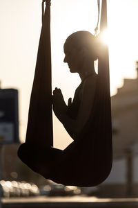 Side view of silhouette woman meditating while sitting on silk at sunset