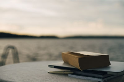 Close-up of laptop with books on table against lake