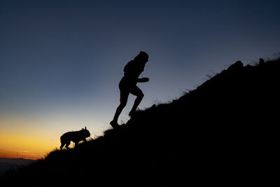 Silhouette woman with dog against sky during sunset