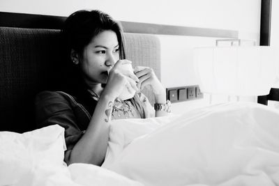 Thoughtful young woman with coffee while relaxing on bed at home