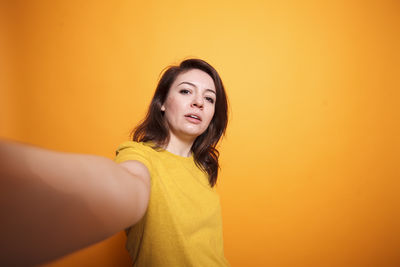 Portrait of young woman standing against yellow background