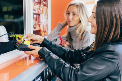 Two attractive girlfriends buying fast food and paying in eat market in the street.