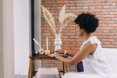 Profile view of woman writing, sitting on a couch against wall