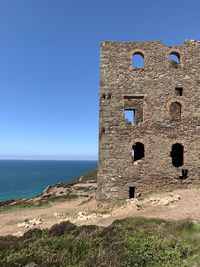 Old building by sea against clear blue sky