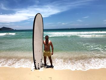 Full length of shirtless man standing at beach against sky