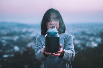 Young woman holding jar while standing against sky during sunset