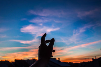 Silhouette cropped hand gesturing against sky during sunset