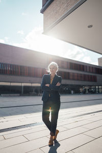 Businesswoman with arms crossed standing on footpath at office park