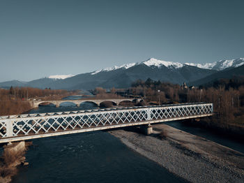 Scenic view of bridge over river against snowcapped mountains and clear sky