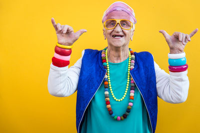 Portrait of smiling senior woman gesturing against yellow background