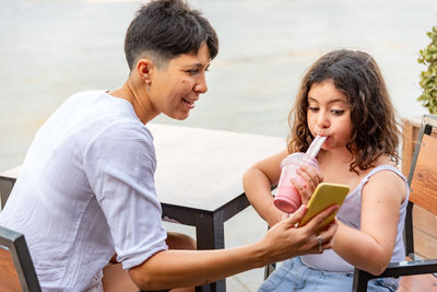 Mother and daughter drinking milkshake and looking at the mobile phone