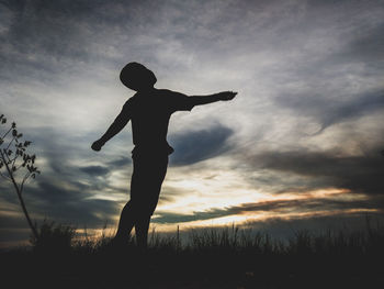 Silhouette boy standing on field against sky