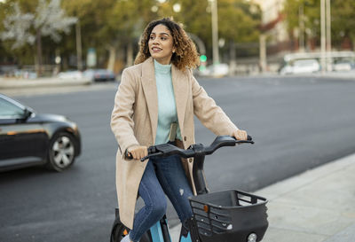 Smiling woman riding electric bicycle on footpath