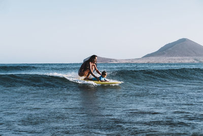 Full view of mother and son surfing a small wave at sea