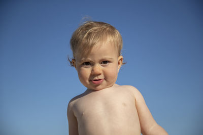 Portrait of shirtless cute baby girl against clear blue sky