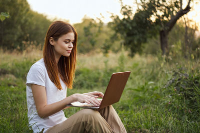 Young woman using digital tablet while sitting on field