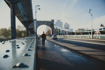 Man walking on bridge against sky in city