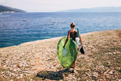Rear view of woman with pool raft walking at beach