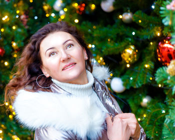 Portrait of a joyful woman in warm clothes on the street near a christmas tree with illumination