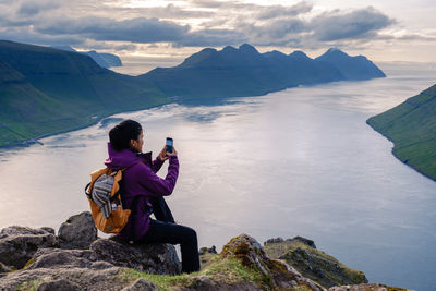 Rear view of woman sitting on rock against mountain