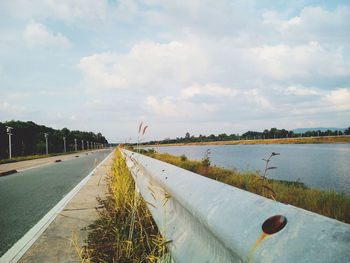 Empty road by lake against sky