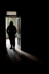 Rear view of silhouette man standing against door at night