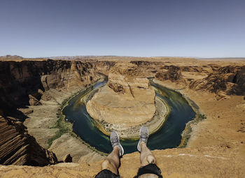 Rear view of man standing on rock formations in desert against clear sky