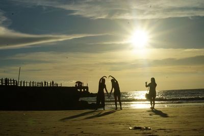 Silhouette people on beach against sky during sunset