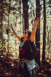 Side view of woman with arms raised standing in forest