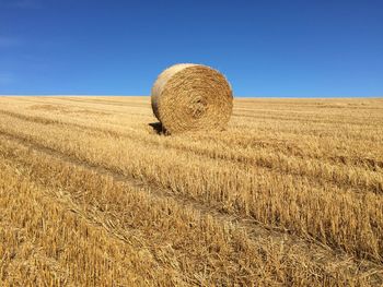 Hay bale on field against clear blue sky