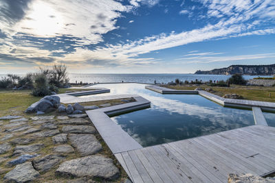 Swimming pool by lake against sky