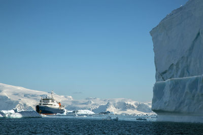 Expedition ship next to a huge iceberg on a sunny day in antarctica.