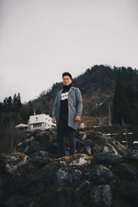 Portrait of young man standing on rock against sky