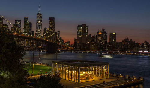 Illuminated modern buildings by river against sky at night