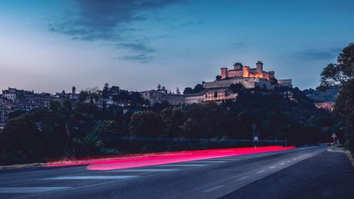 Light trails on road amidst buildings in city at dusk