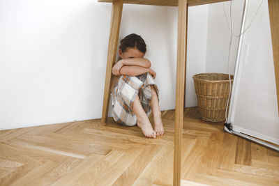 Depressed little girl sitting under table on floor at home