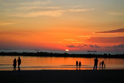 Silhouette people on shore at beach against sky during sunset