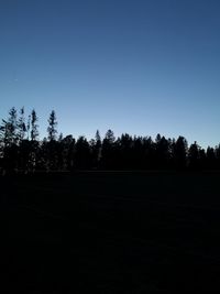 Silhouette trees on field against clear sky