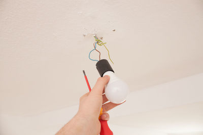 Cropped hand of man adjusting light bulb on ceiling at home