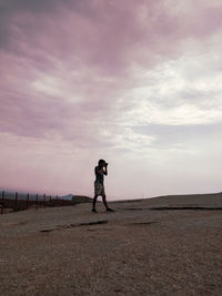 Full length of woman standing on land against sky during sunset