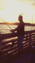 Rear view of man fishing at sunset