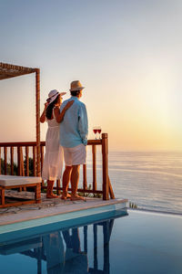 Rear view of men standing by swimming pool against sky