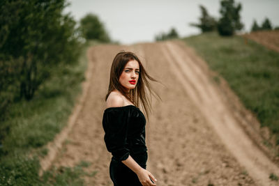 Portrait of young woman standing on dirt road