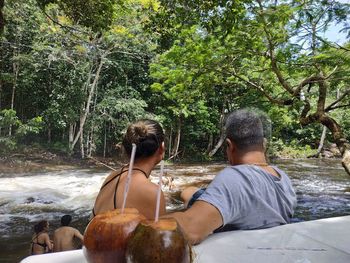 Rear view of friends sitting by river in forest
