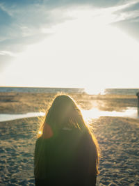 Rear view of woman standing at beach against sky