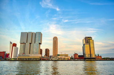 Modern buildings by river against sky in city