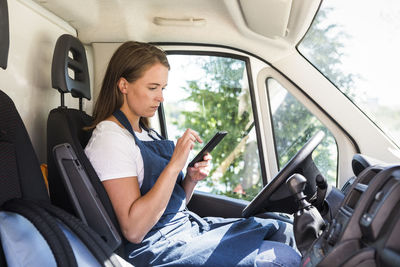 Side view of confident young female owner using smart phone while sitting in food truck