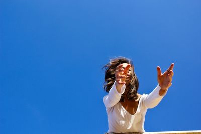 Low angle view of woman standing against clear blue sky