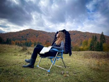 Rear view of woman sitting on field against sky